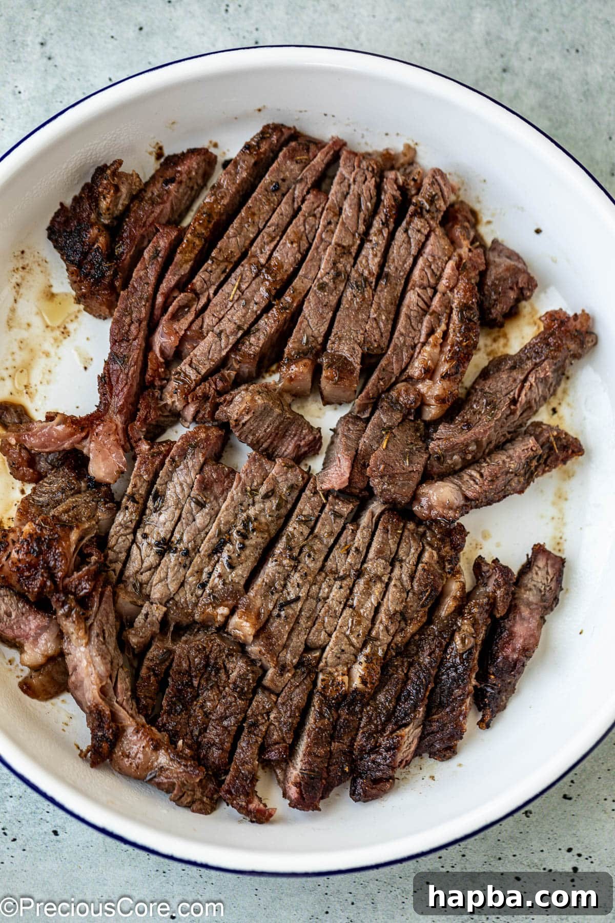 Cooked ribeye steak, thinly sliced against the grain on a cutting board, revealing its juicy interior.