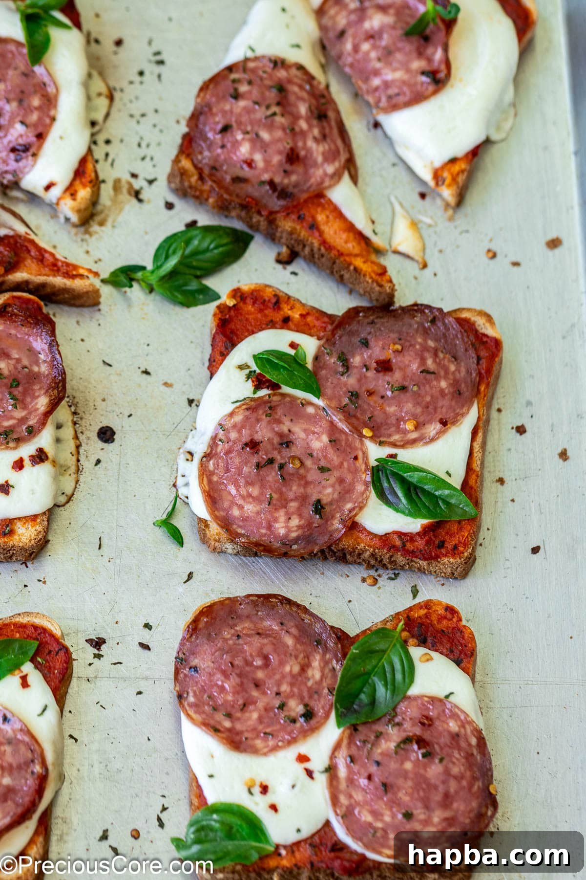 Close-up view of several golden-brown pizza toasts arranged on a baking sheet, showcasing melted cheese and toppings.