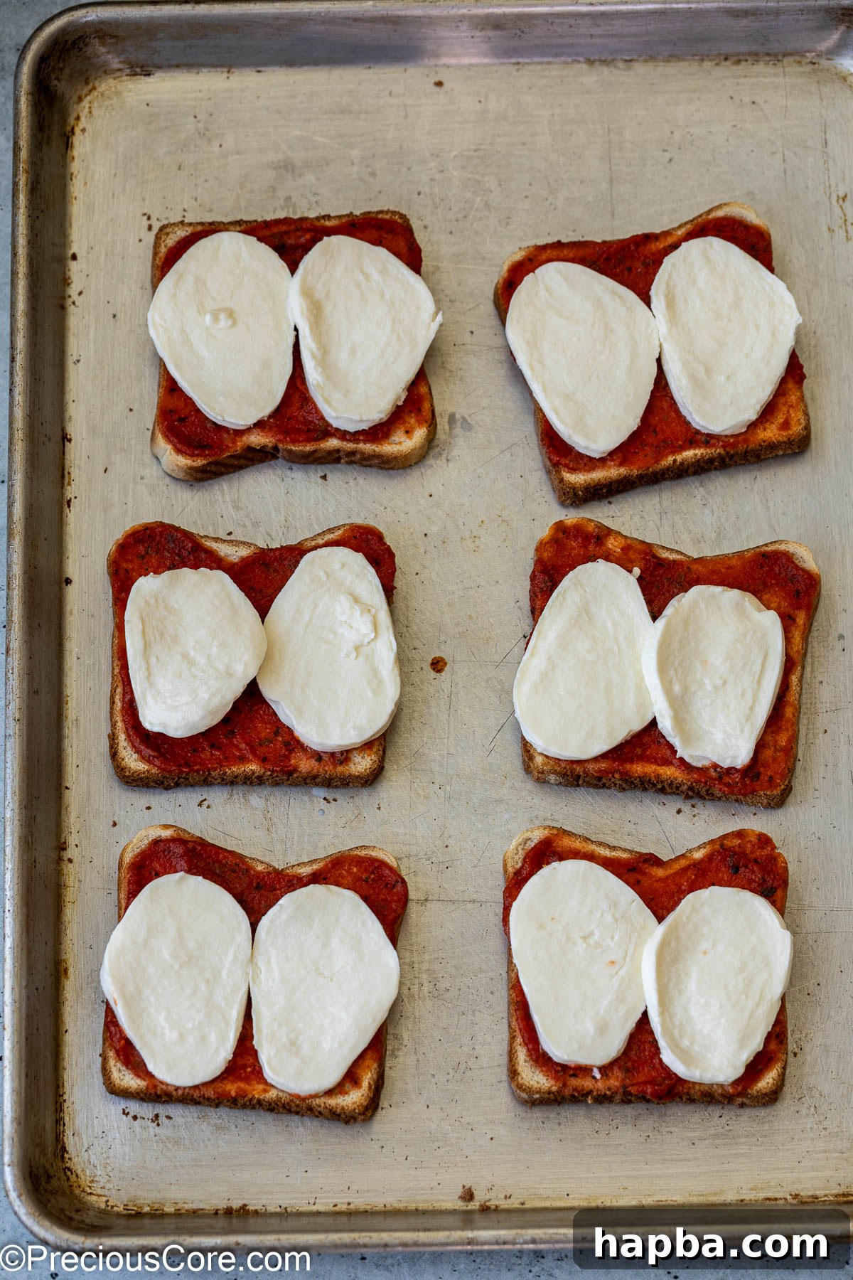 Fresh mozzarella cheese slices carefully placed on top of sauced bread slices.