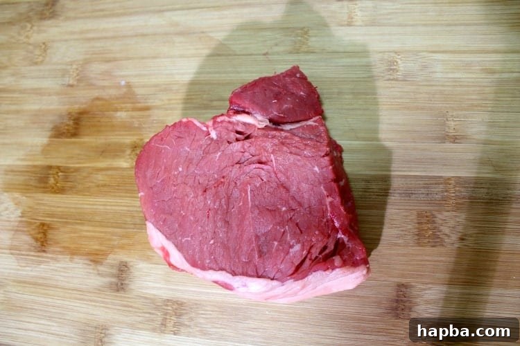 Piece of top sirloin steak on a wooden cutting board, ready for slicing.