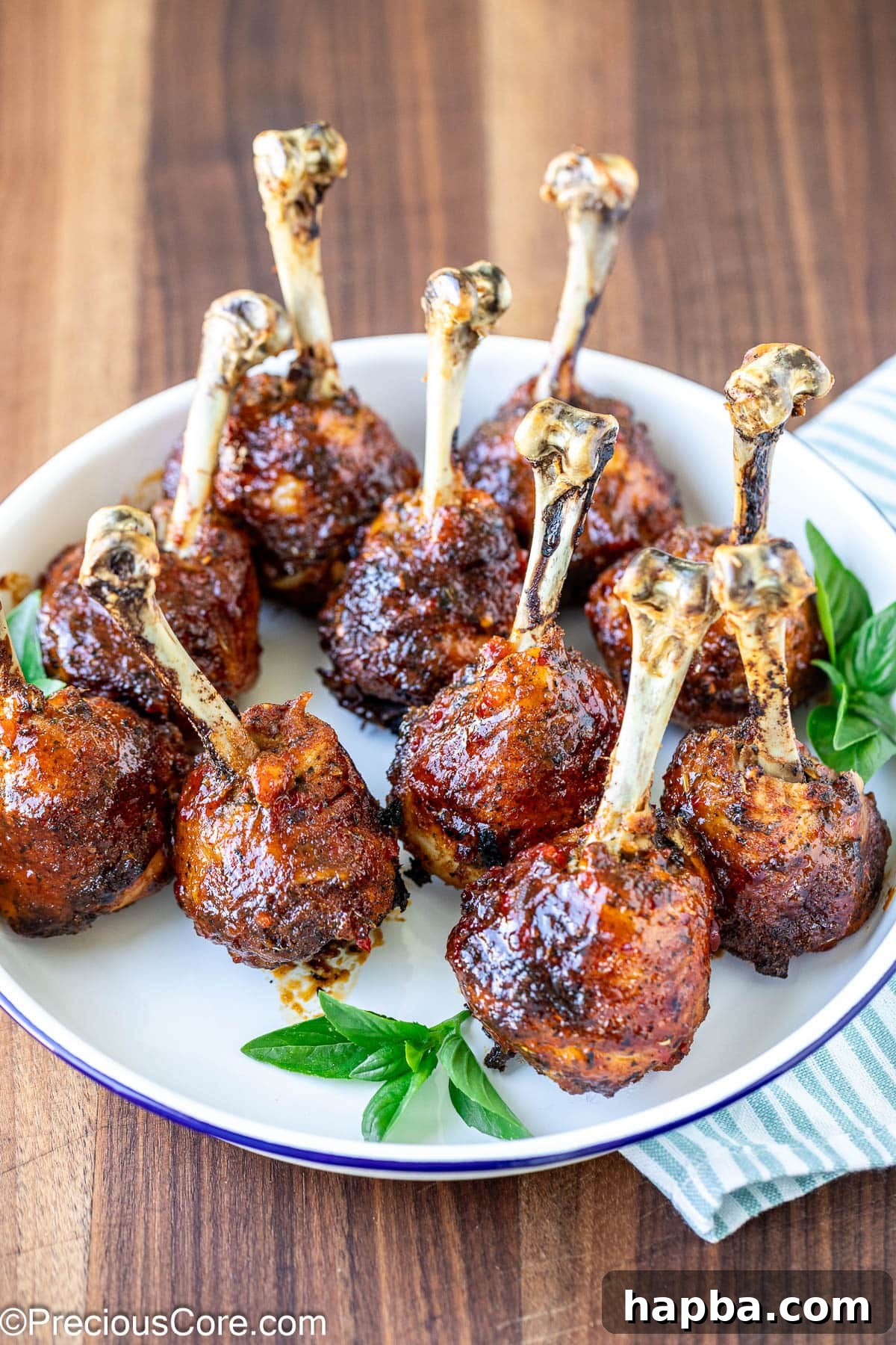Plate of baked and glazed chicken lollipops, garnished with fresh herbs.