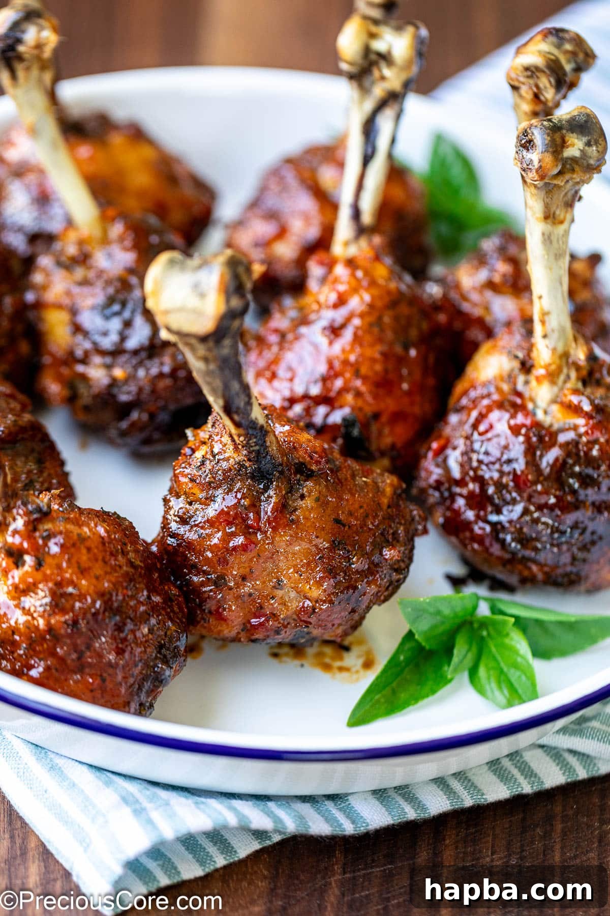 Beautifully glazed chicken drumstick lollipops on a plate, garnished with fresh herbs.