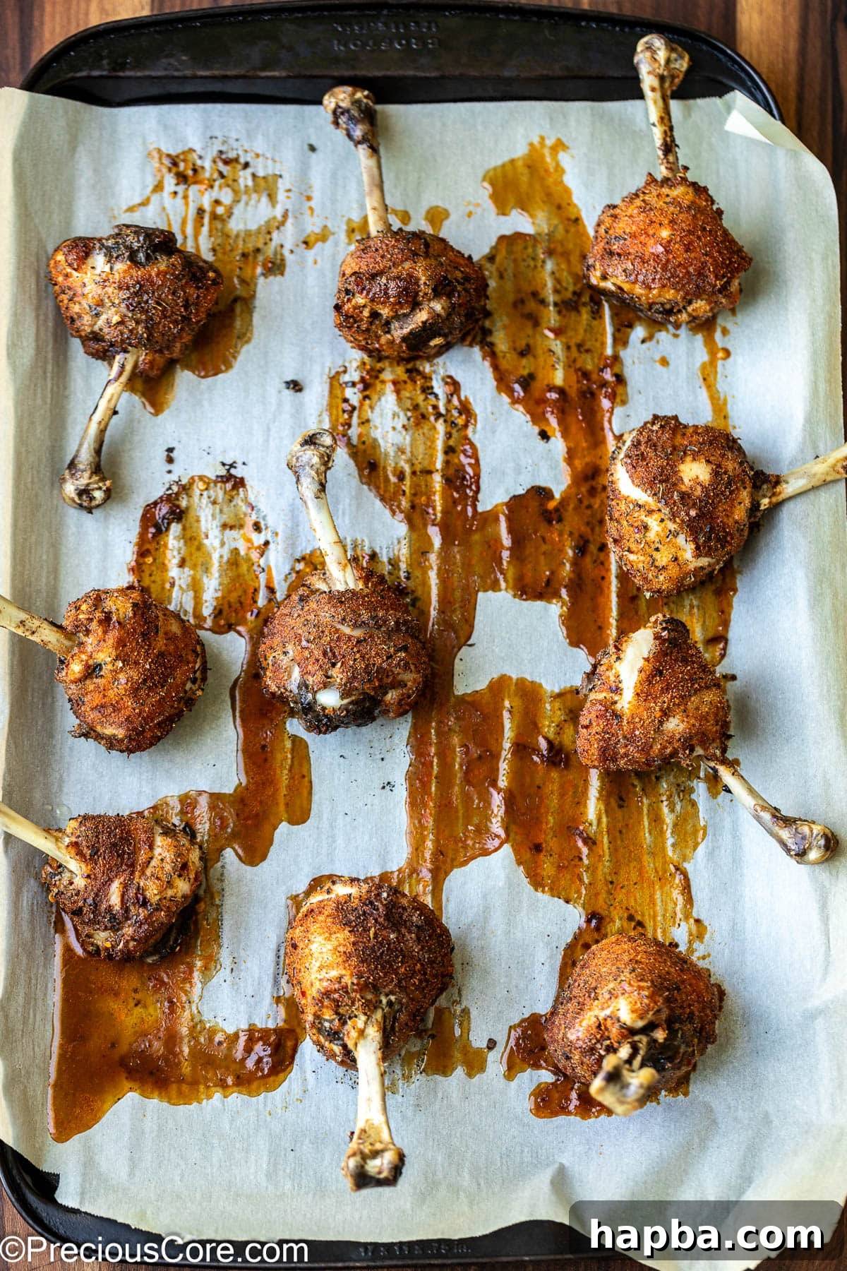 Partially baked chicken drumstick lollipops on a baking sheet, golden brown.
