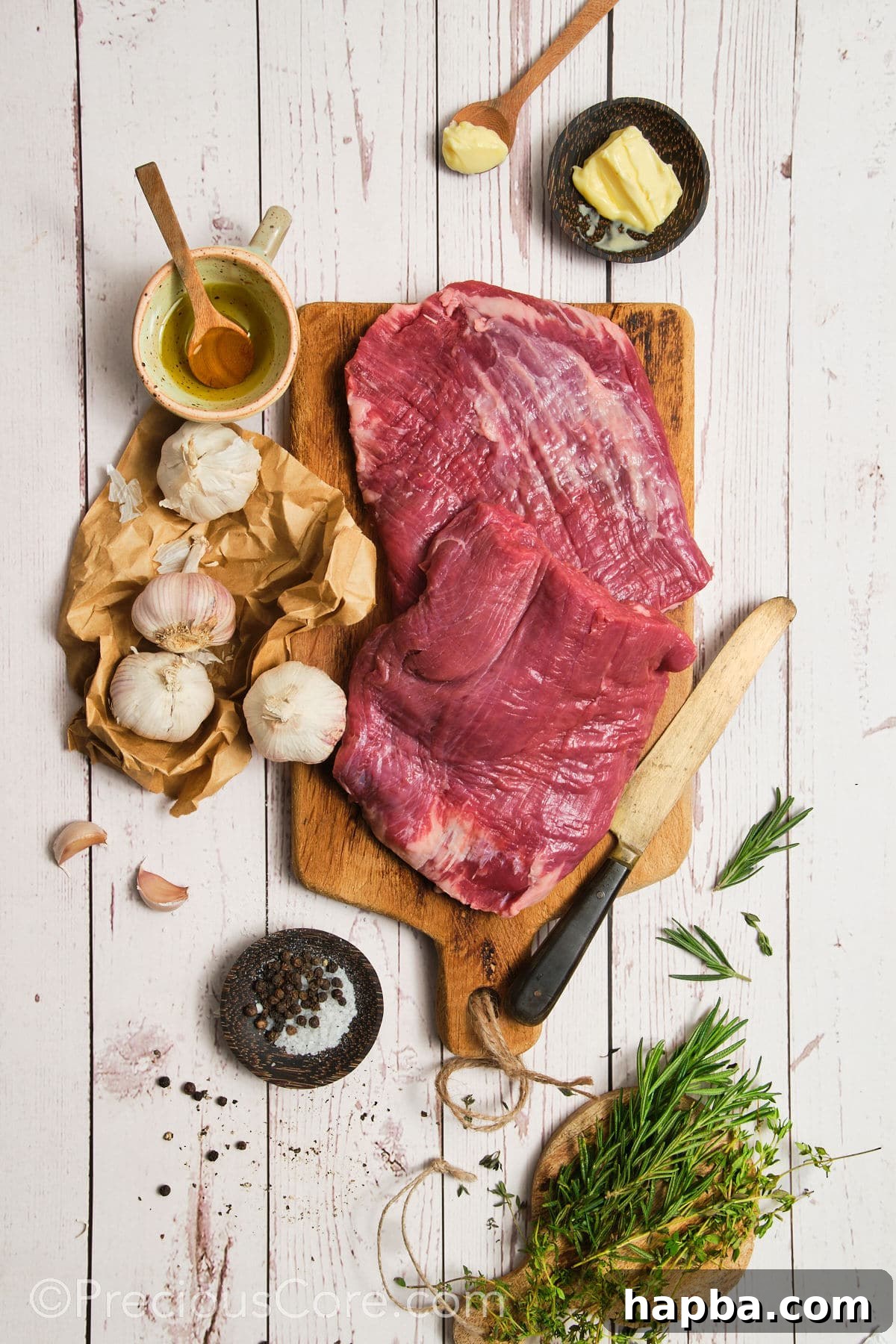 A vibrant flat lay of fresh ingredients, including flank steak, garlic cloves, sprigs of rosemary and thyme, olive oil, and butter, ready for pan-searing.