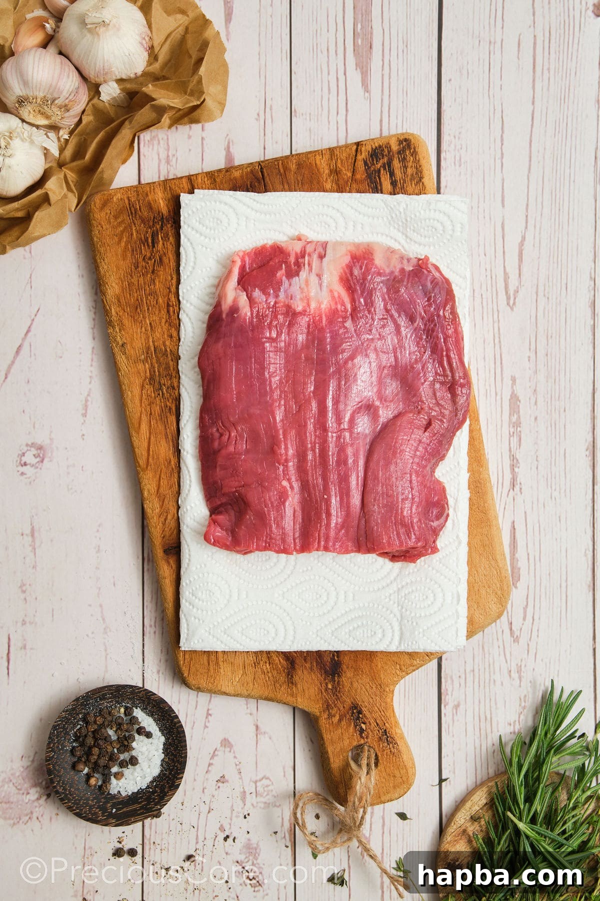 Hands carefully patting dry a piece of flank steak with paper towels, ensuring all surface moisture is removed for an optimal sear.