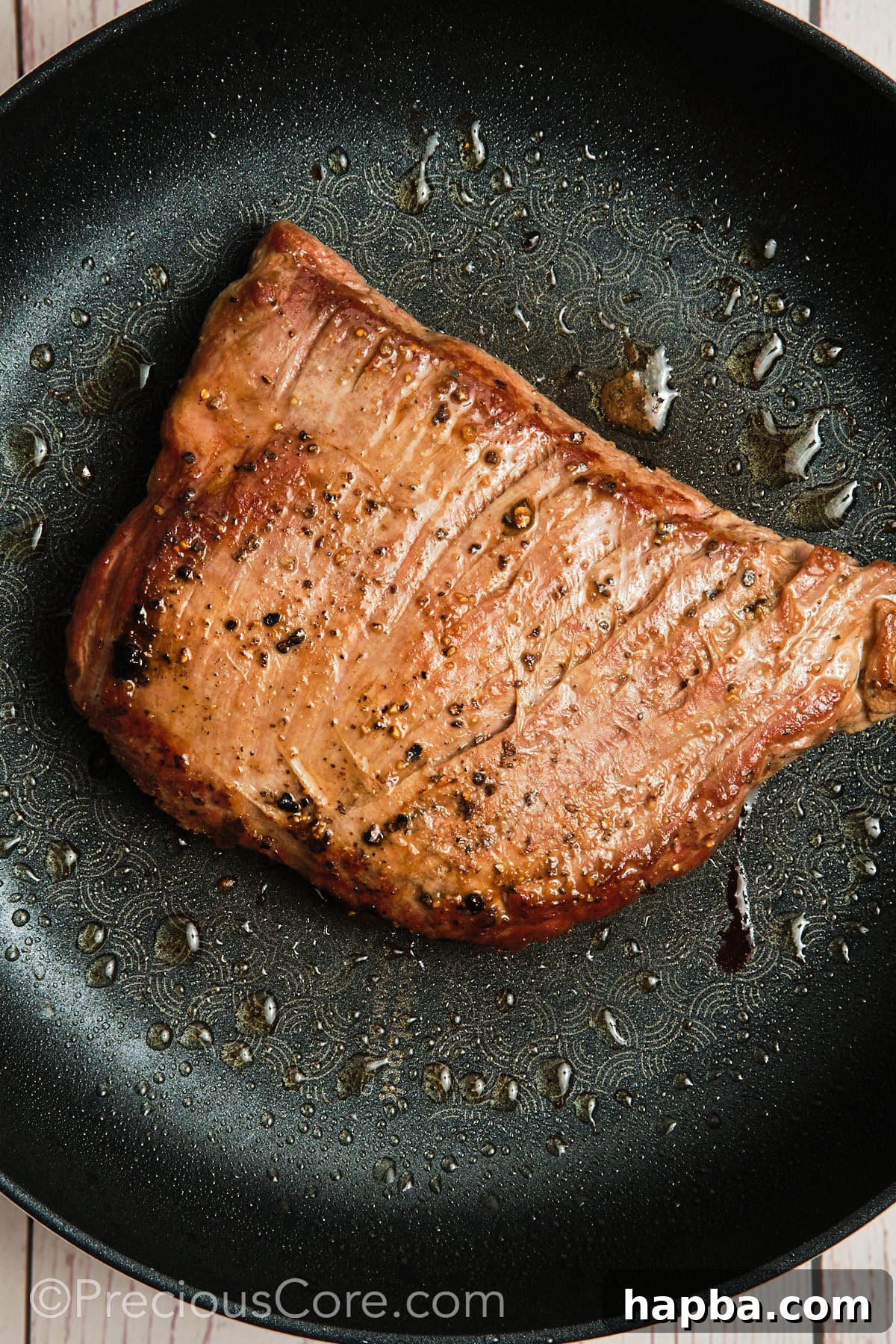 A piece of flank steak sizzling in a hot skillet, developing a golden-brown crust during the searing process.