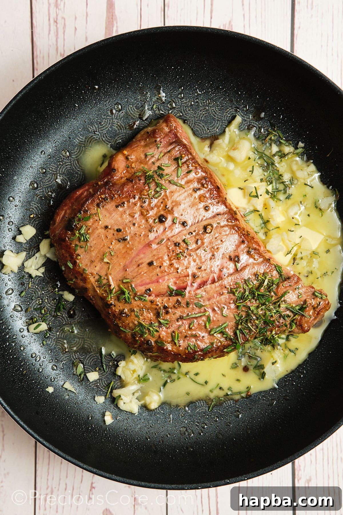 Melted butter dotted around the sizzling flank steak in the pan, ready for garlic and herbs to be added.