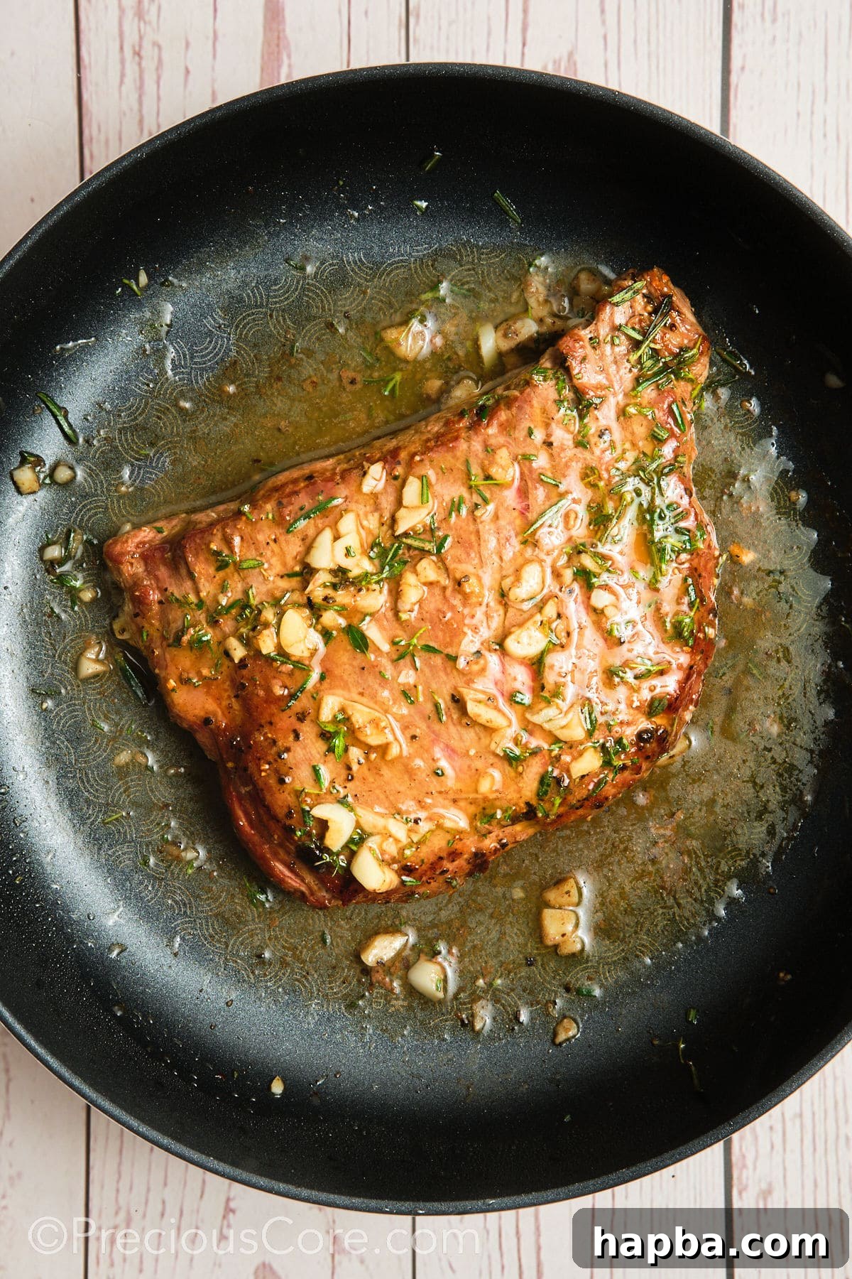 Pan-seared flank steak being generously basted with a rich garlic herb butter sauce, enhancing its flavor and juiciness.