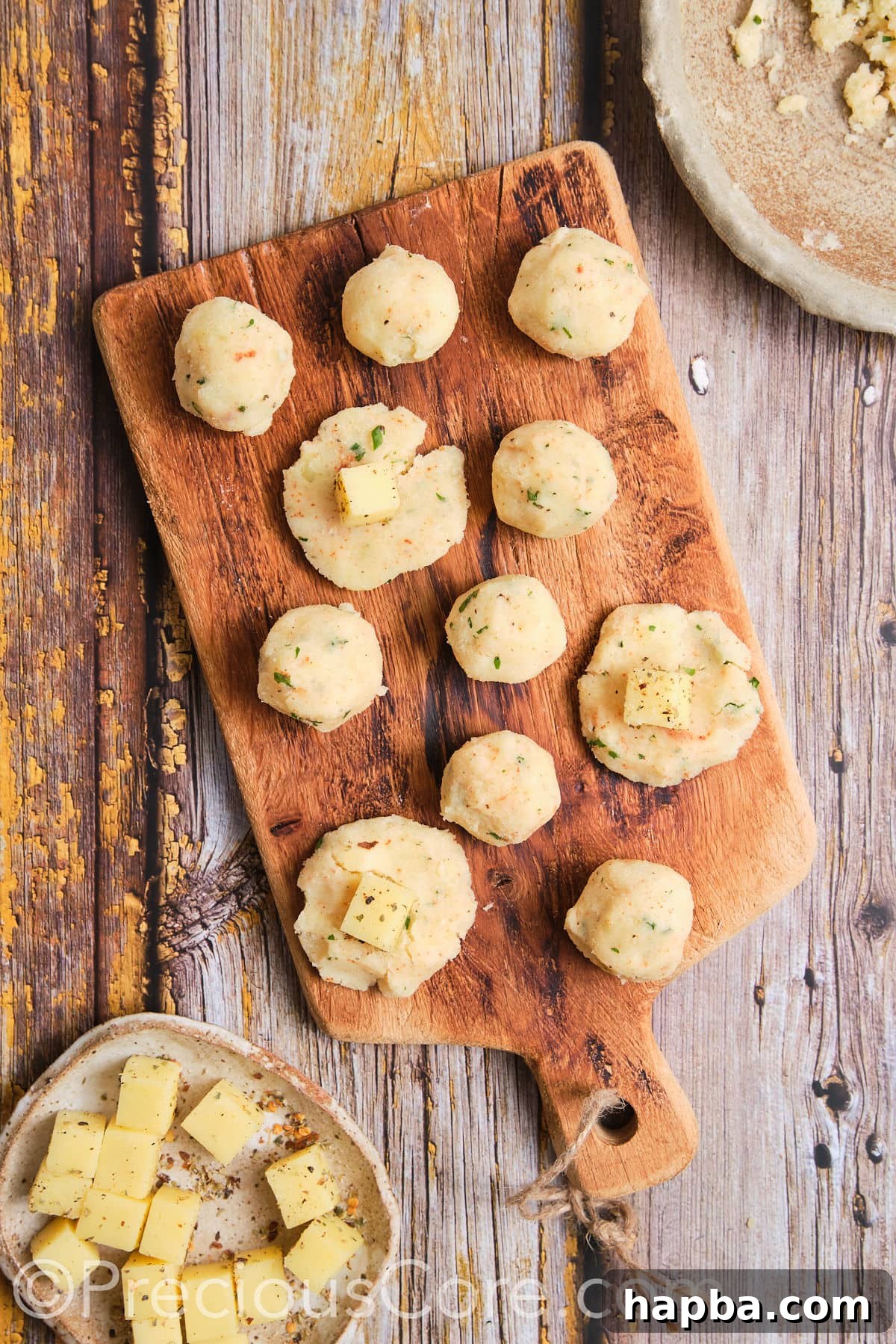 Adding cheese cubes to mashed potato balls.