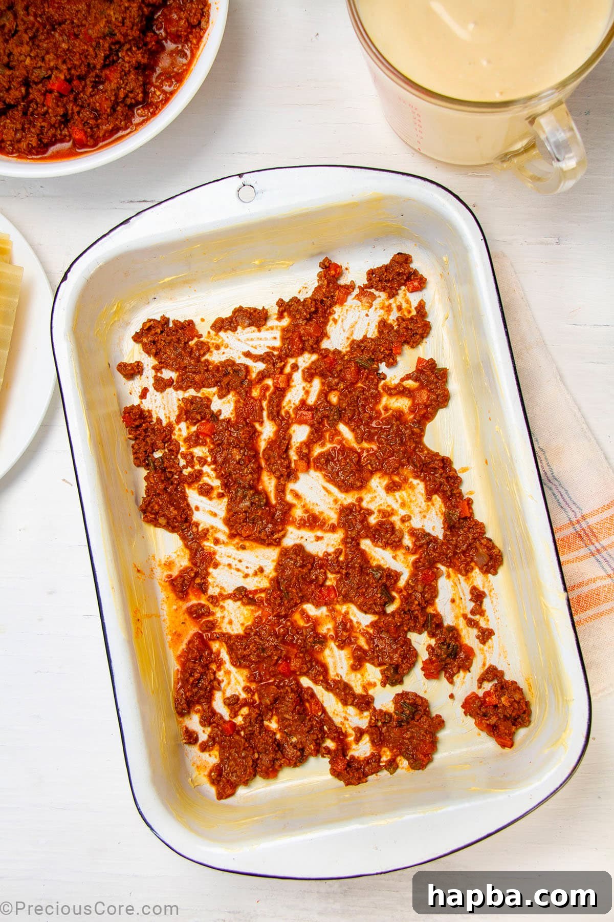 Creamy Béchamel Lasagna 12 A baking dish with a thin layer of rich Bolognese meat sauce spread evenly across the bottom, preparing for the first layer of pasta.
