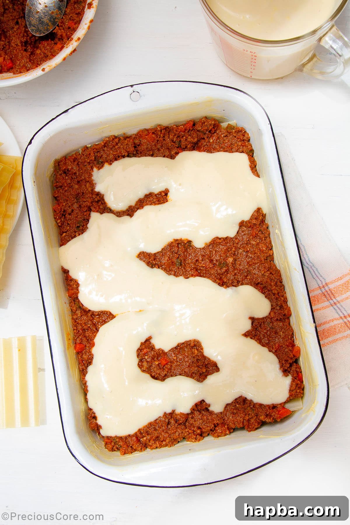 Creamy Béchamel Lasagna 14 A layer of creamy béchamel sauce spread over the Bolognese meat sauce in a baking dish, creating a smooth white top layer.