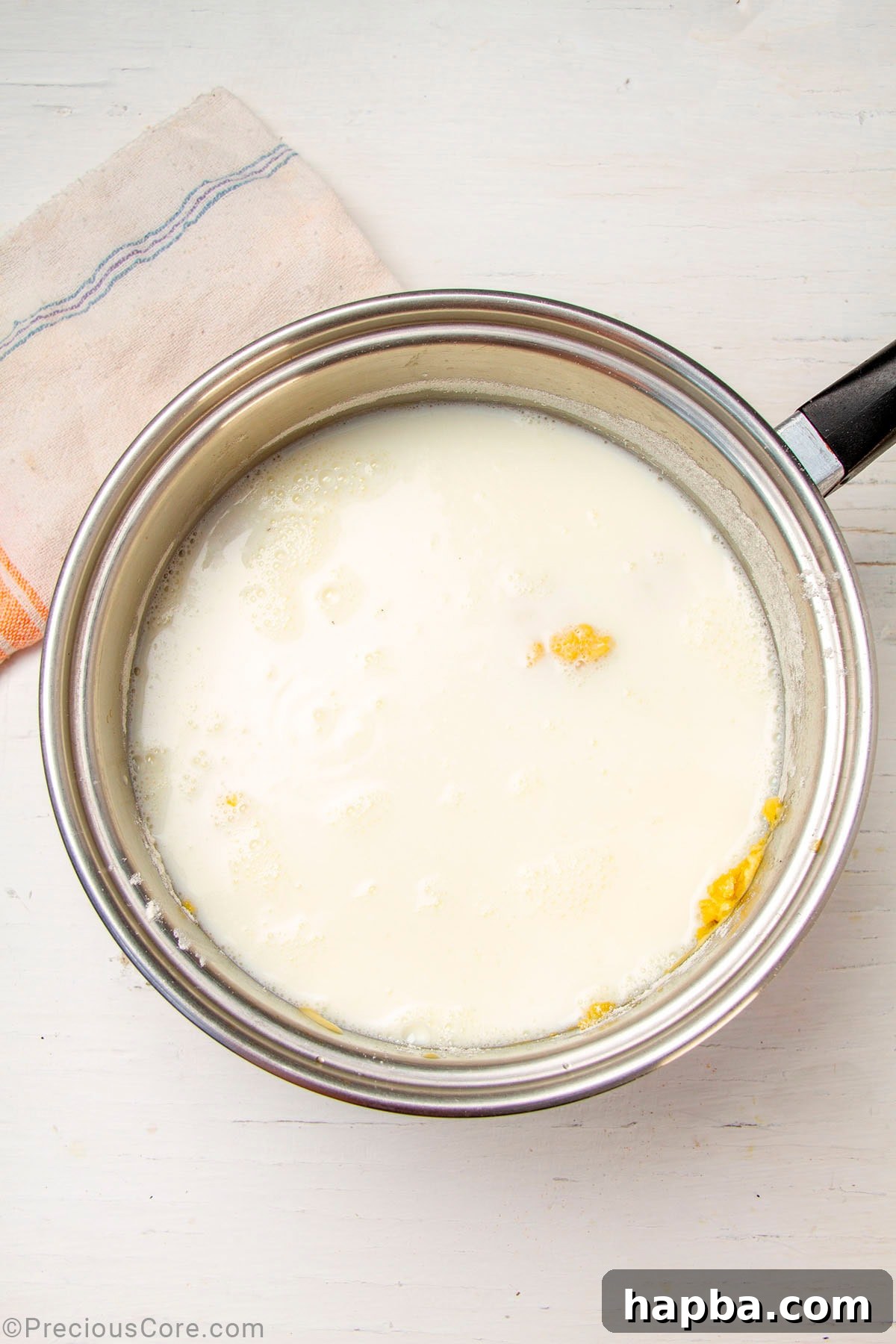 Creamy Béchamel Lasagna 9 Warm milk being poured into a saucepan containing a roux, with a whisk actively stirring the mixture to combine.