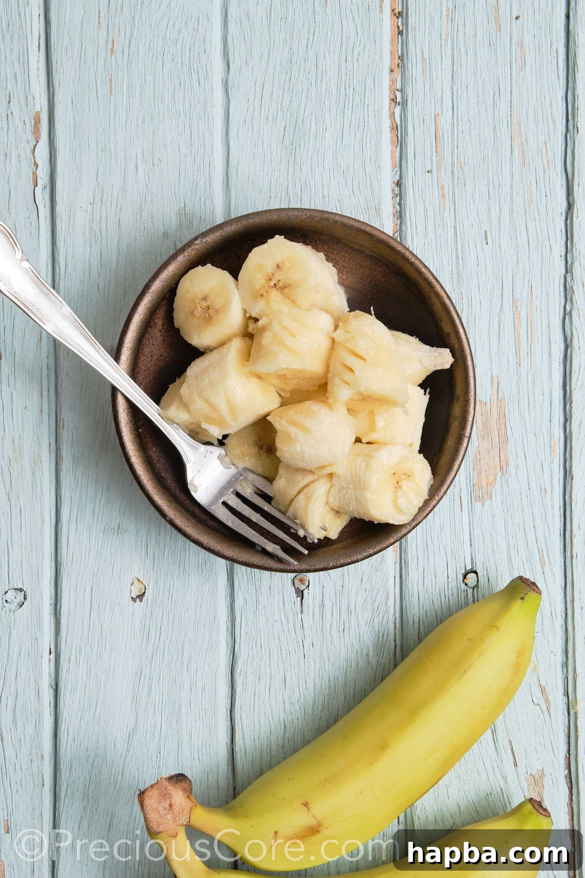 A hand mashing bananas in a bowl with a fork, showing the initial preparation step.
