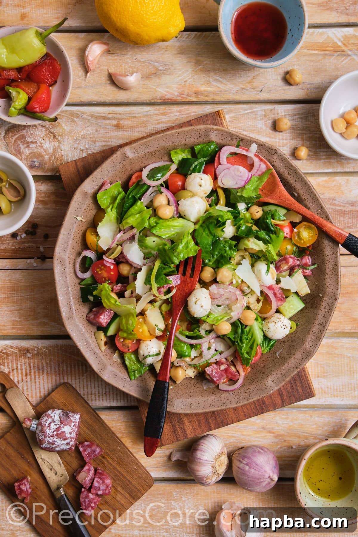 A chef's hands gently mixing the ingredients of an Italian Chopped Salad in a large glass bowl.