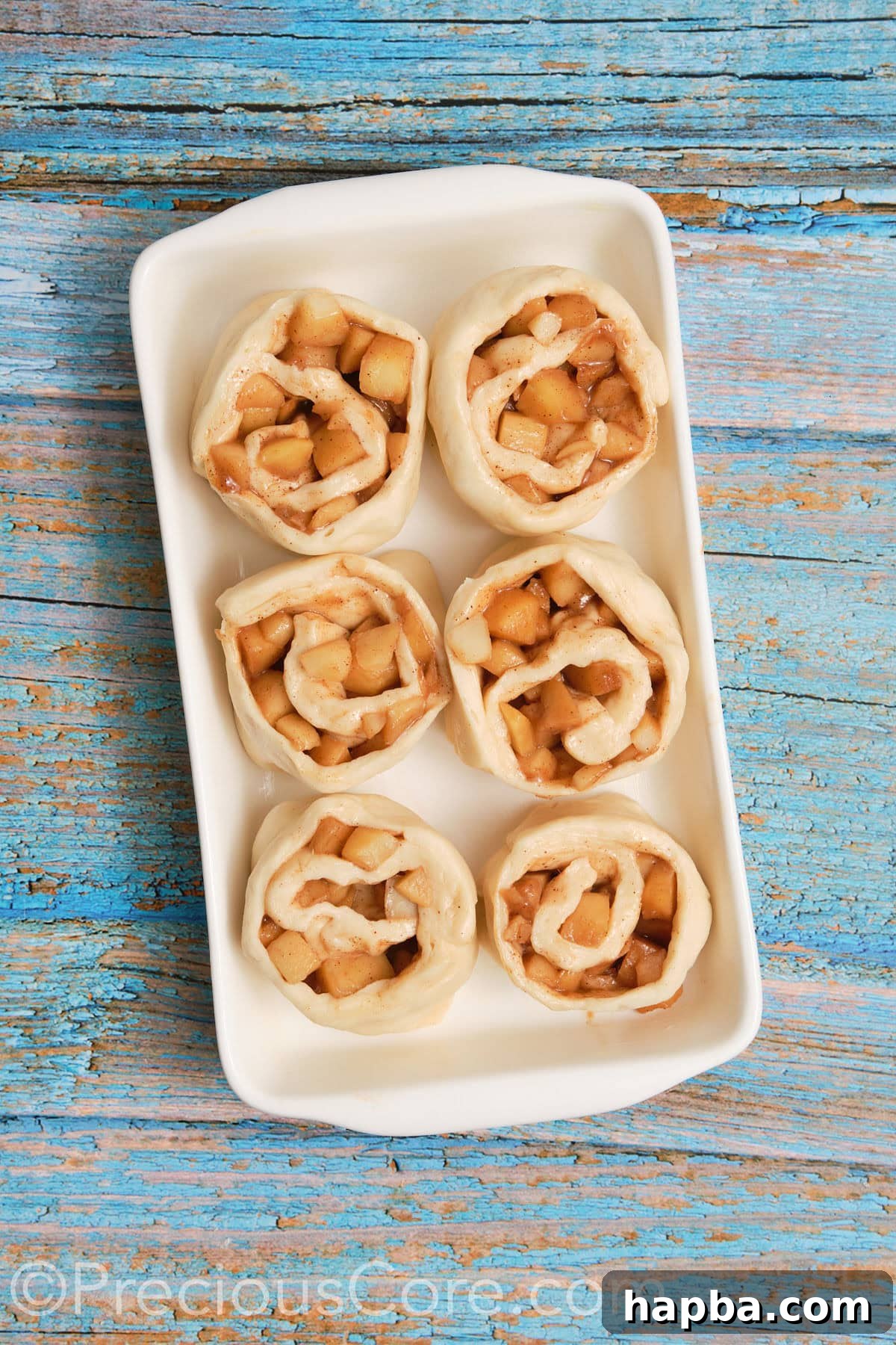 Assembled cinnamon apple rolls carefully placed into a buttered casserole dish, ready for their second rise.