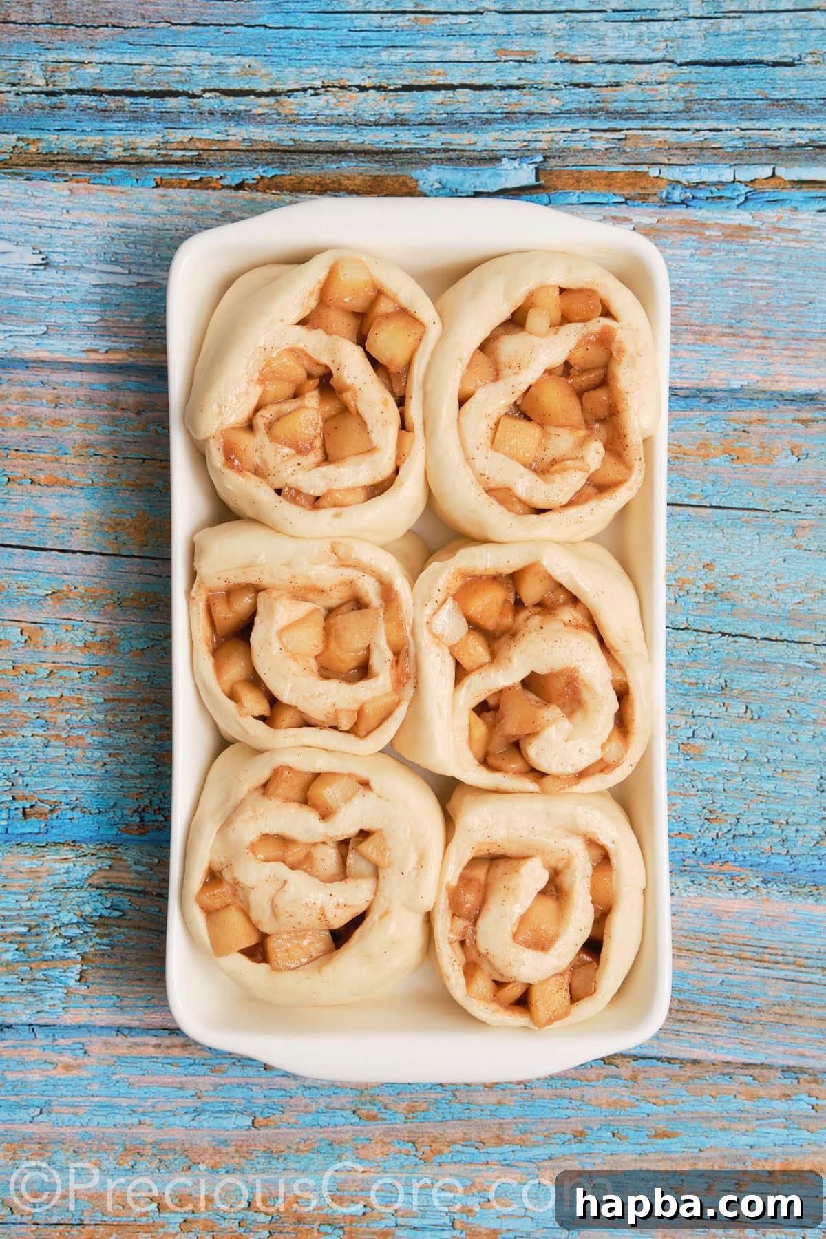 Puffed-up cinnamon apple rolls after their second rise, filling the baking dish and ready for the oven.
