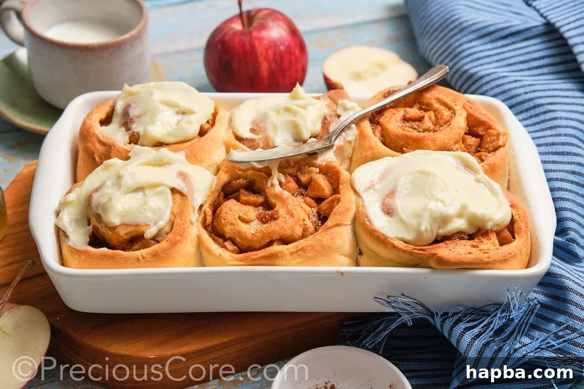 Six beautifully baked cinnamon rolls with apple pie filling arranged in a baking dish, perfectly golden and ready to be frosted.