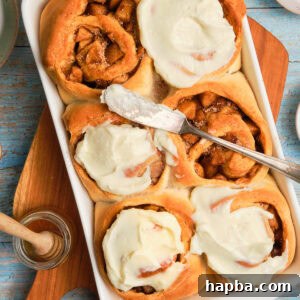 Homemade Cinnamon Rolls filled with apple pie filling, topped with a generous layer of cream cheese frosting.