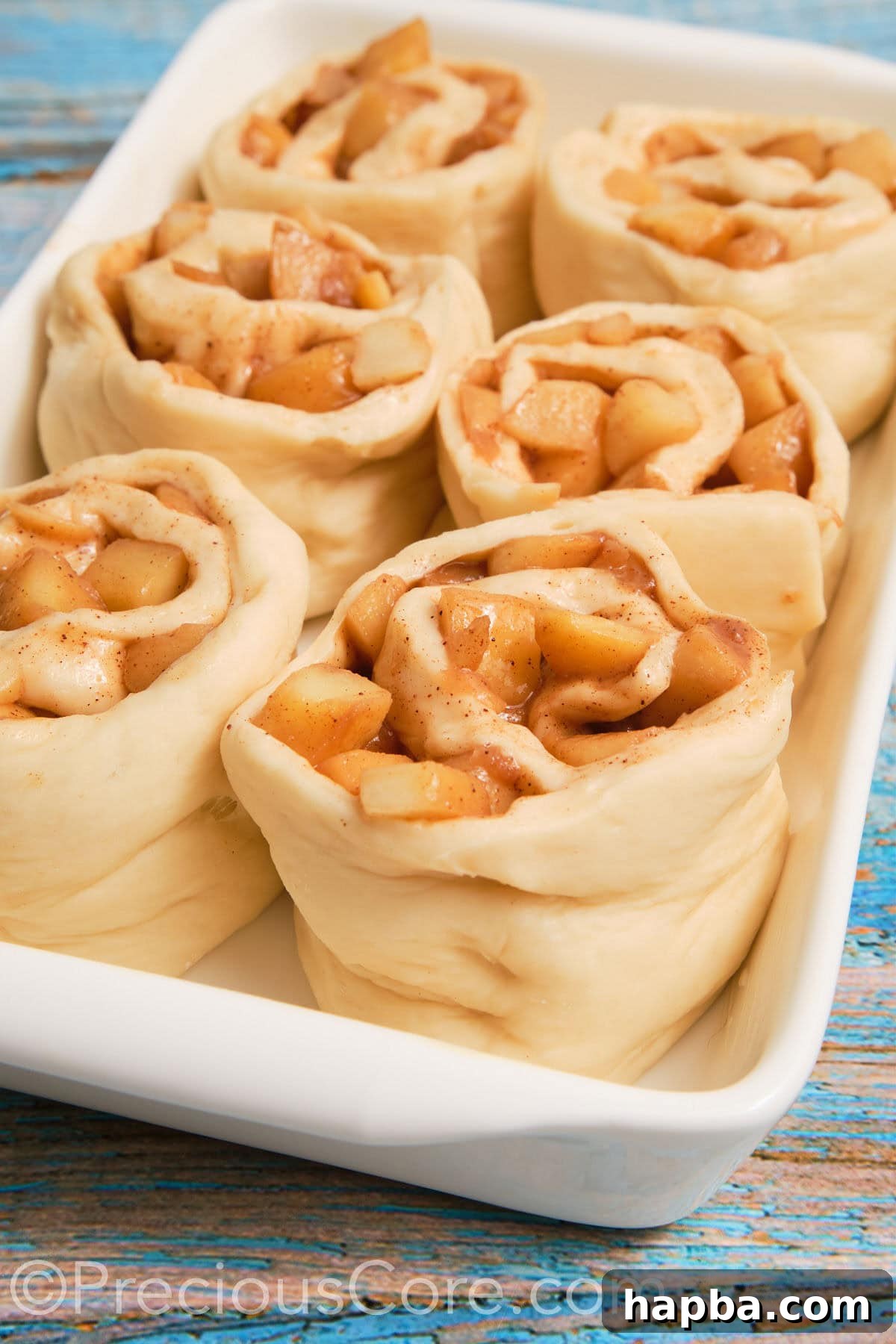 Close-up of the cinnamon roll dough generously filled with spiced apple pie filling, rolled up and ready for slicing.