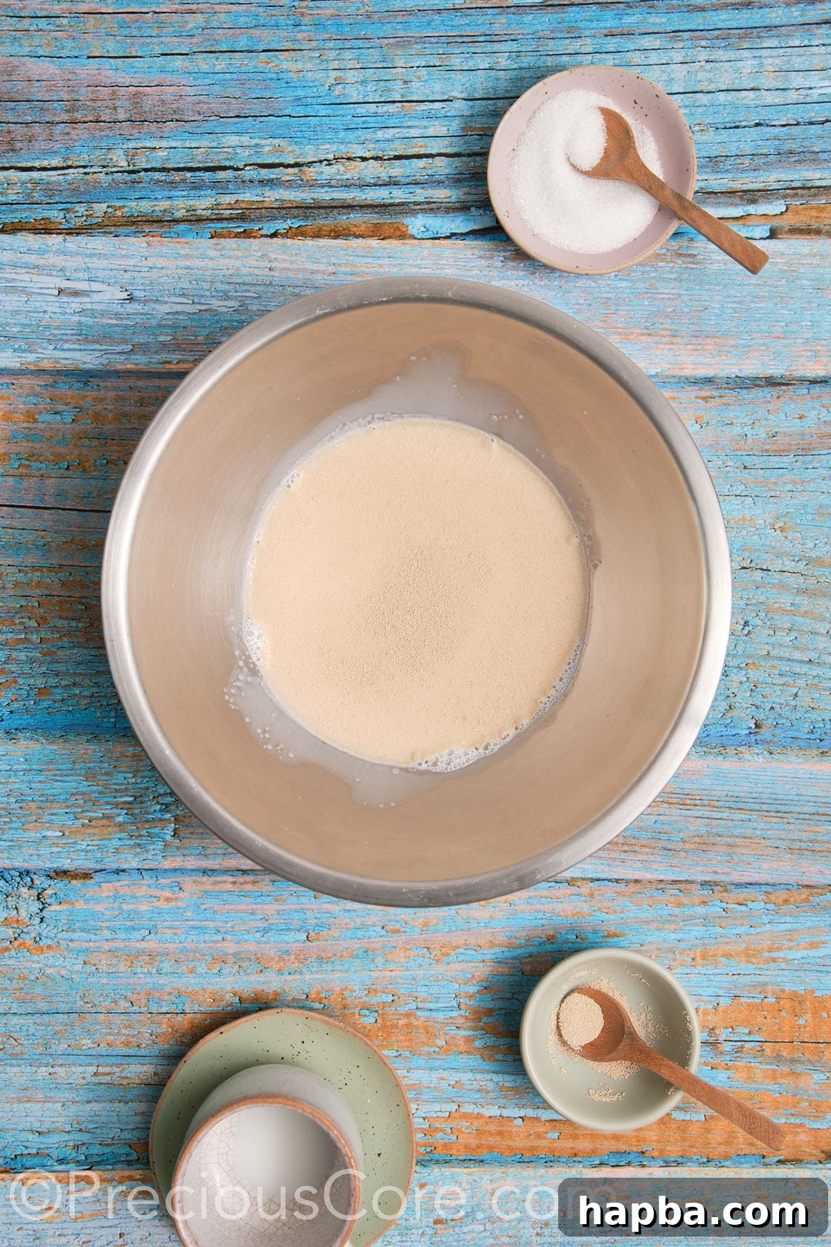 Yeast proofing in a mixing bowl with warm milk, showing a foamy layer on top.