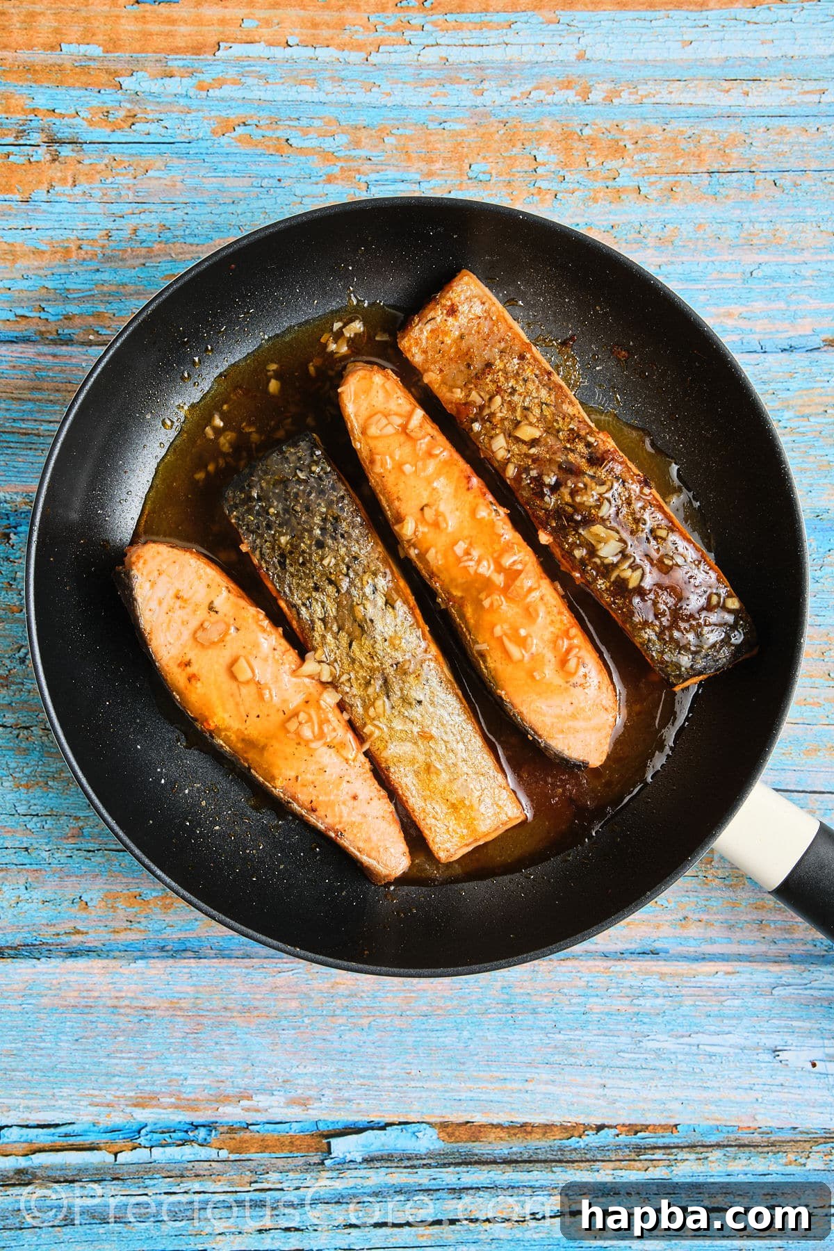 Salmon fillets simmering in the honey butter sauce in a skillet, absorbing all the flavors.