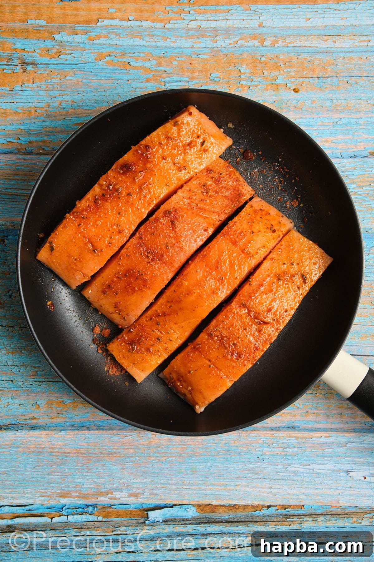 Salmon fillets cooking skin-side down in a hot non-stick skillet, searing to a golden crisp.