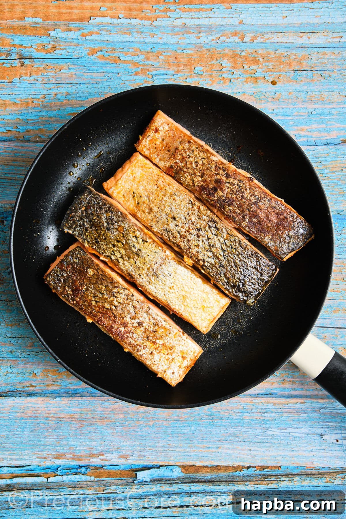Salmon fillets flipped to cook on the flesh side in the skillet.