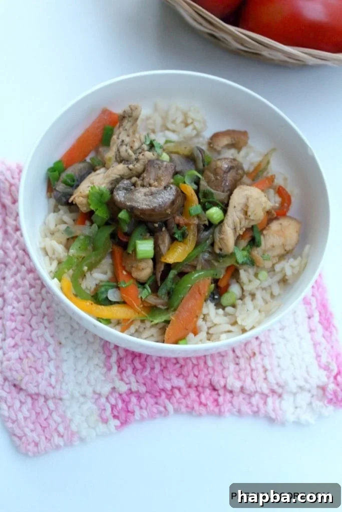Generous serving of chicken and mushroom stir fry over brown rice in a bowl