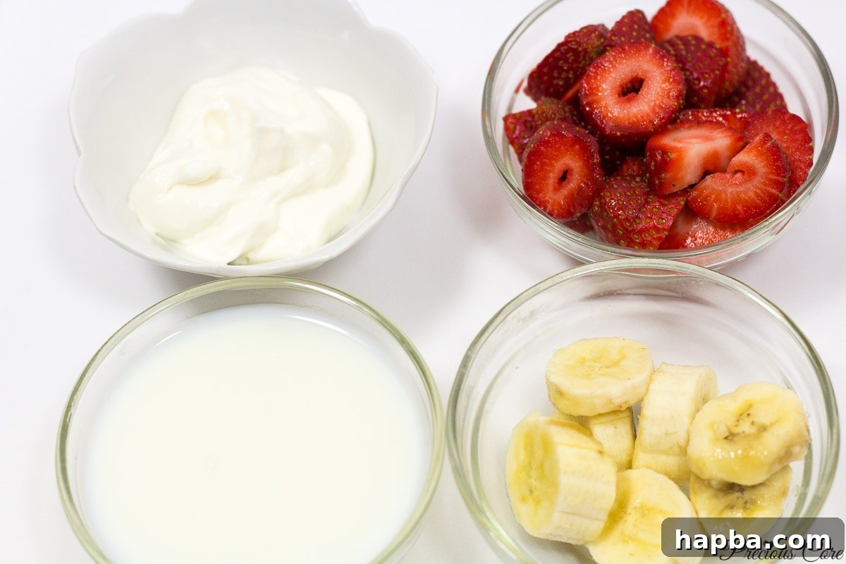 Ingredients for a strawberry-banana smoothie: fresh ripe strawberries, a sliced banana, and a container of yogurt, indicating a wholesome and creamy blend.