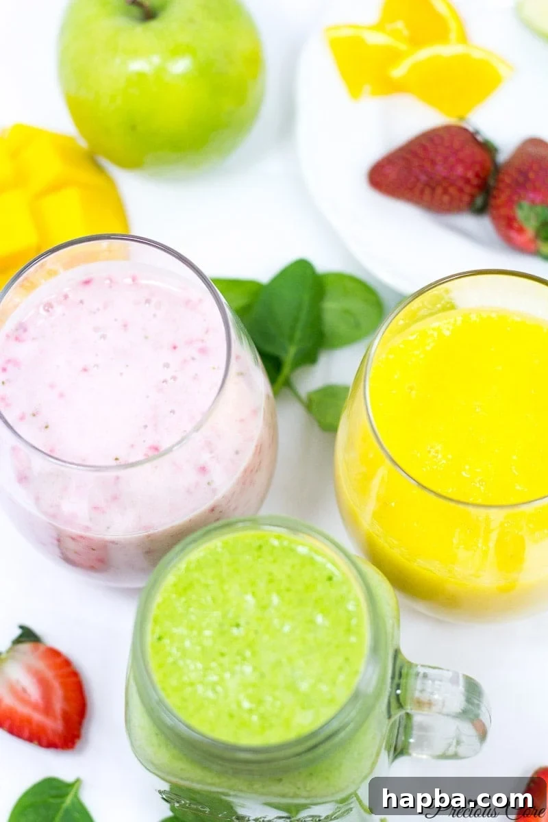 Three distinct smoothies in small glasses, showcasing their vibrant colors: yellow (pineapple mango), green (spinach), and pink (strawberry banana), arranged invitingly.