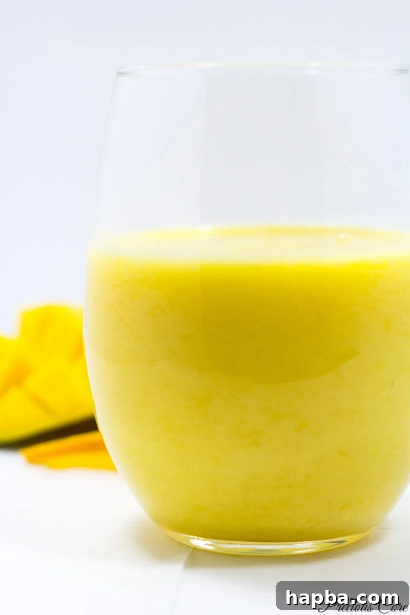 A vibrant yellow pineapple mango smoothie served in a clear glass, garnished with a slice of pineapple, evoking a tropical island feel.