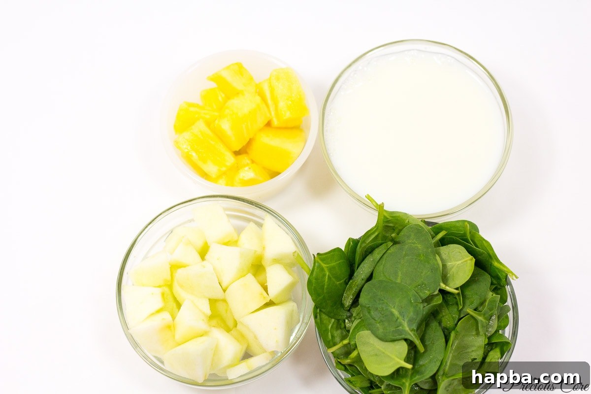 Fresh ingredients for a green smoothie, including a generous bunch of spinach, crisp green apples, and sweet pineapple chunks, laid out on a wooden surface.