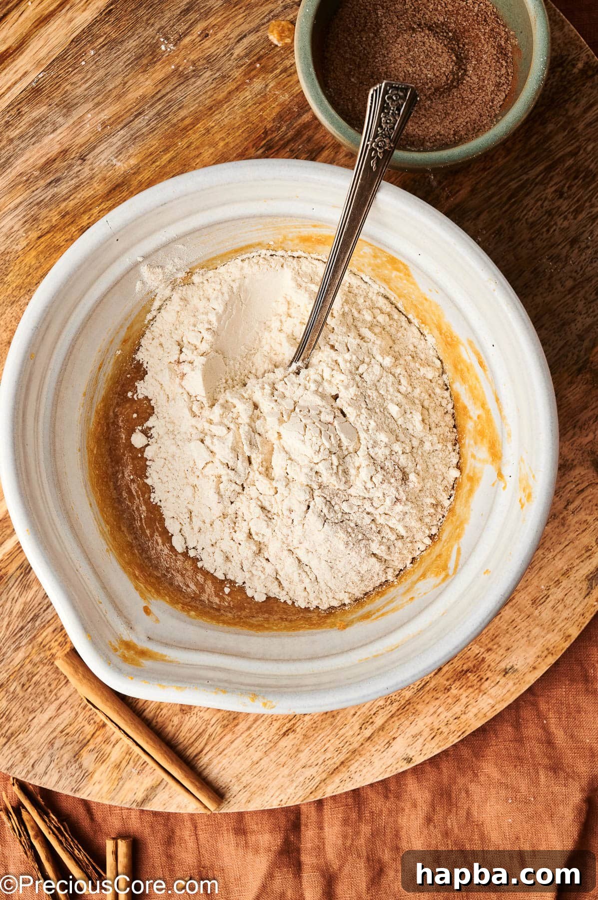 Dry flour mixture being added to the wet pumpkin puree and butter mixture in a large bowl.