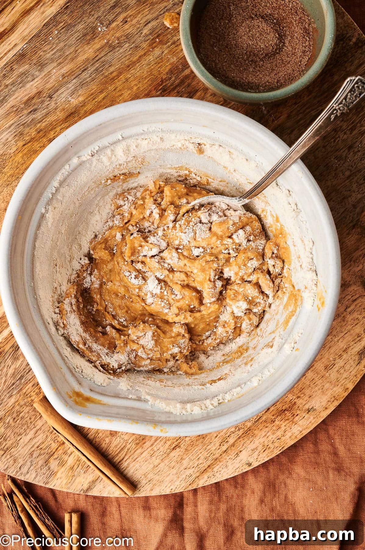 A spatula gently mixing the flour into the pumpkin mixture, forming the doughnut batter.