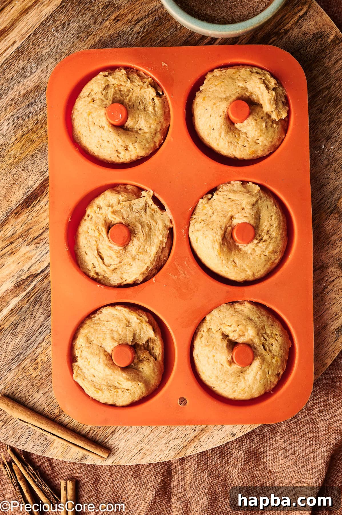 Pumpkin spice batter being neatly piped into a greased doughnut pan, filling each cavity evenly.