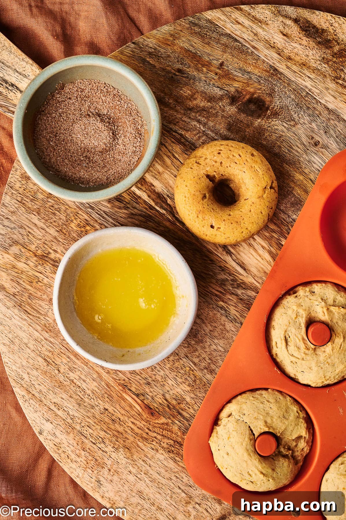 A baked pumpkin doughnut being dipped into melted butter, preparing it for the cinnamon sugar coating.
