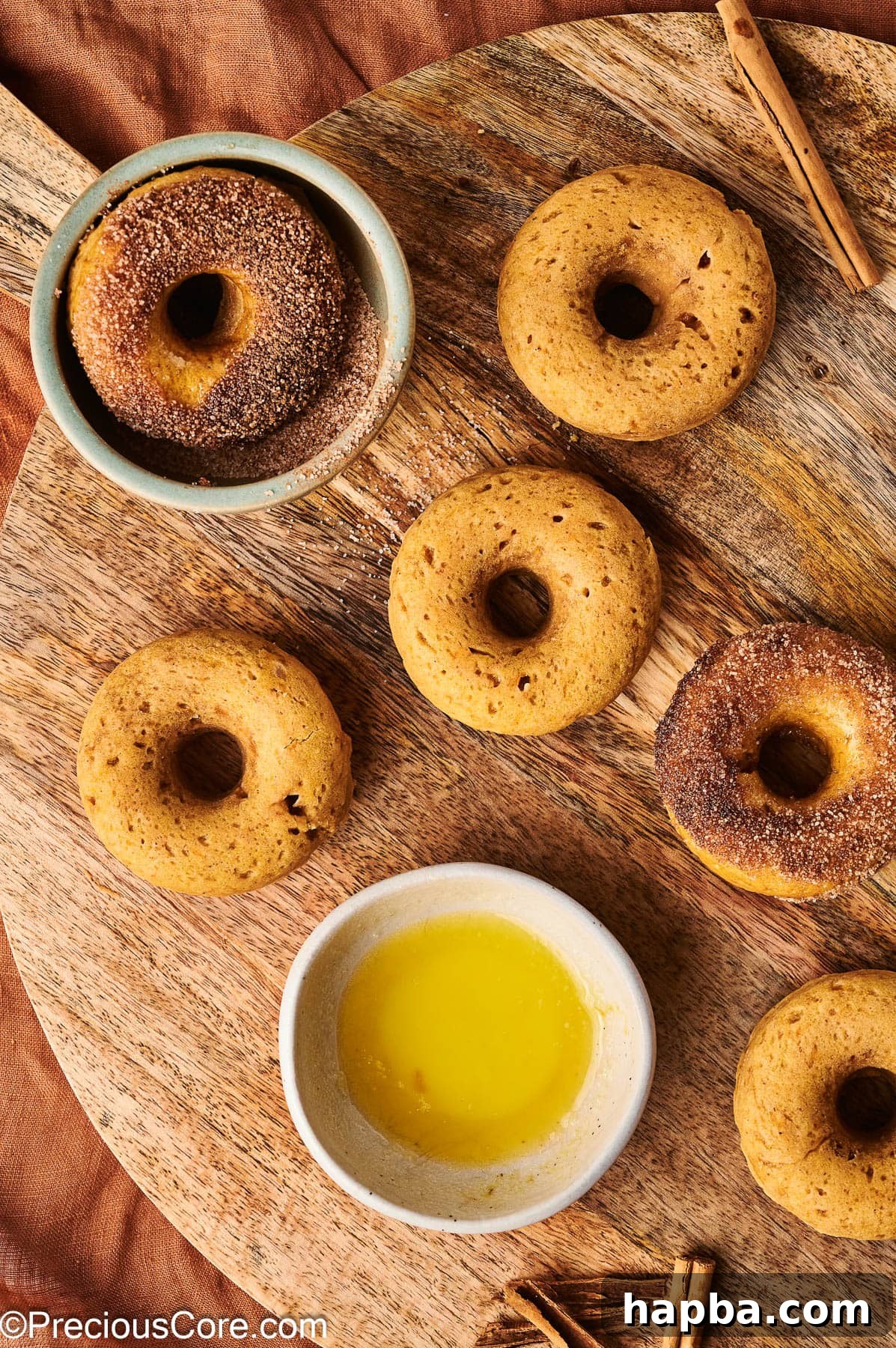 Two pumpkin doughnuts, one fully coated in cinnamon sugar and another partially coated, on a plate.