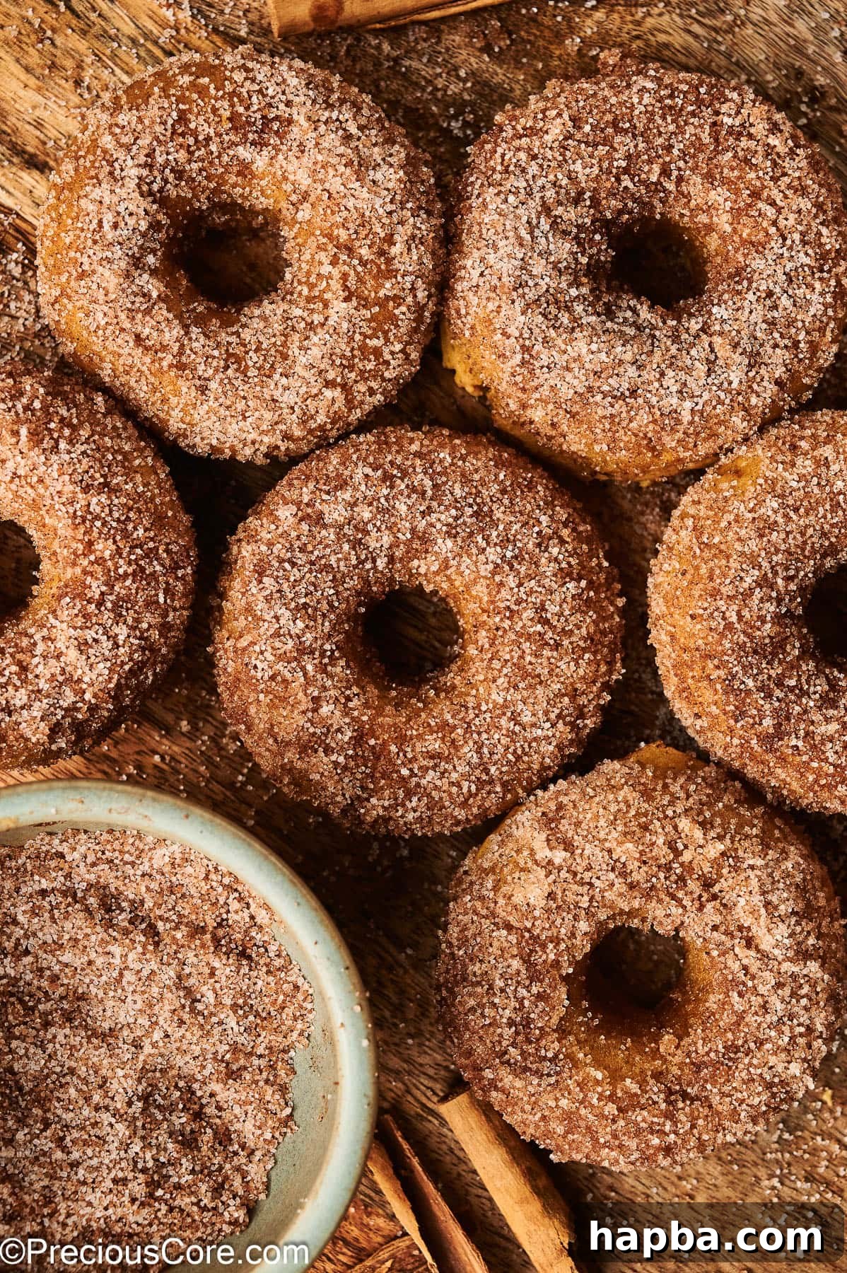 A close-up shot of golden-brown cinnamon sugar pumpkin doughnuts arranged on a wooden board, highlighting their texture.