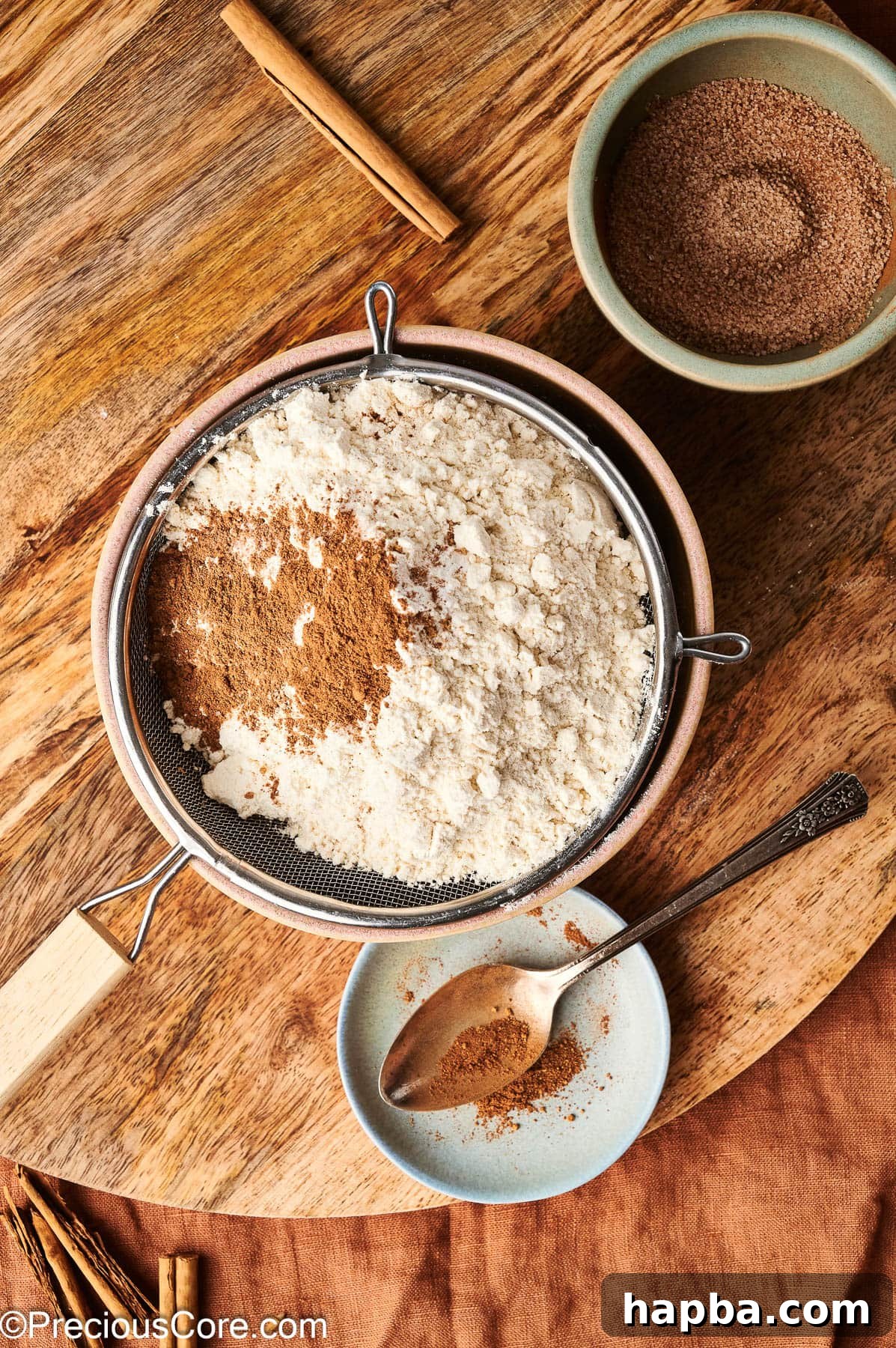 A hand holding a fine mesh sieve, sifting flour and other dry ingredients into a mixing bowl.