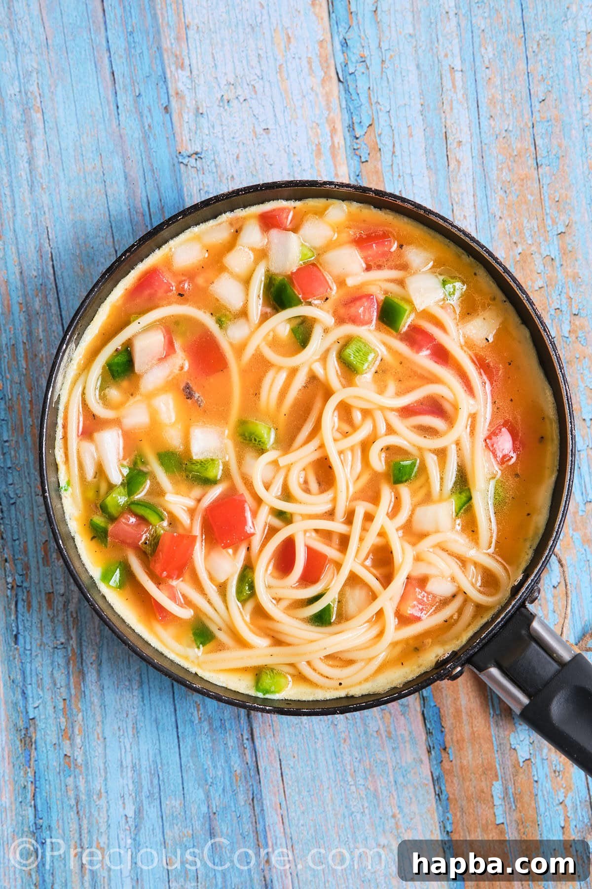 A fluffy spaghetti omelette gently cooking in a medium skillet, achieving a perfect golden hue.