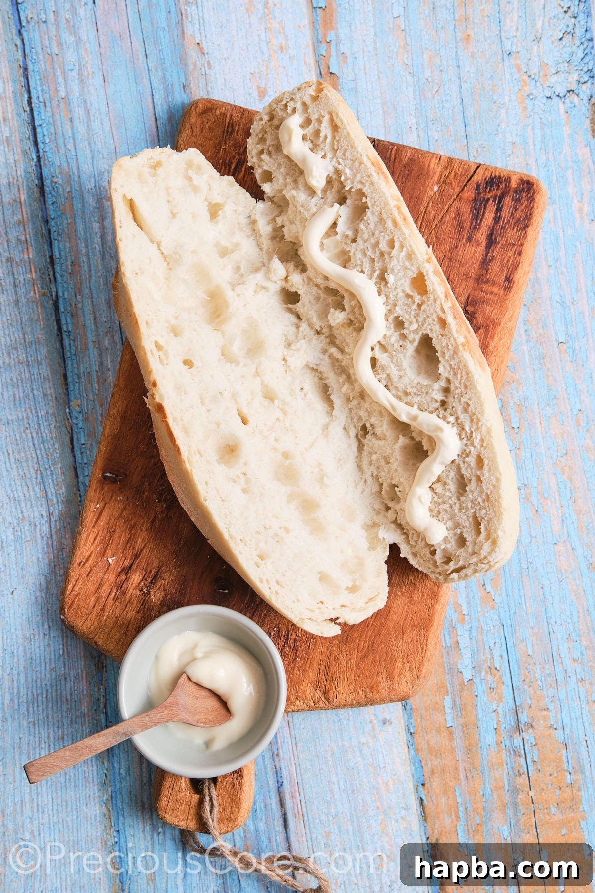 Creamy mayonnaise drizzled generously on one side of a split baguette, ready for filling.