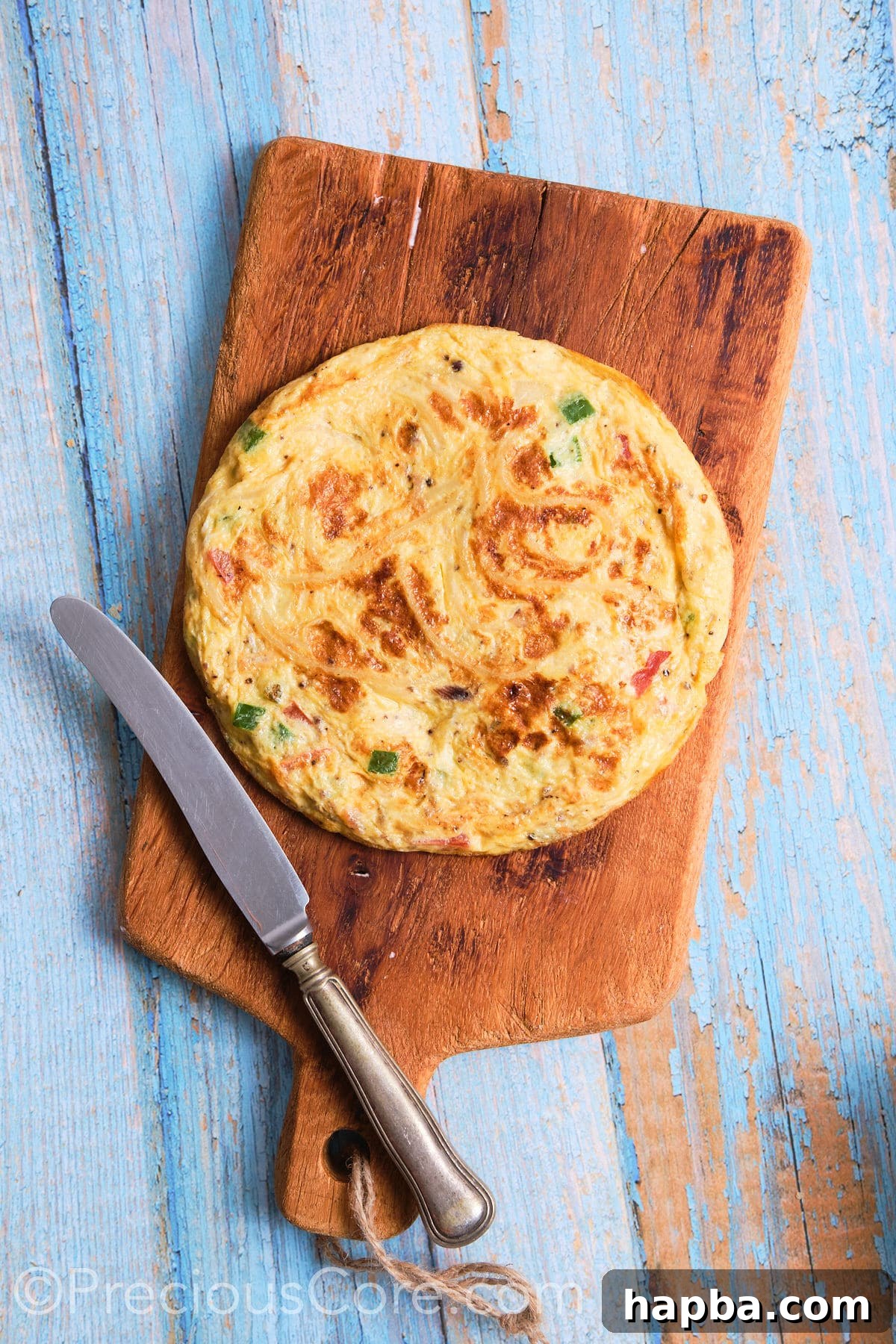 A freshly cooked spaghetti omelette, removed from the skillet and resting on a cutting board, ready to be sliced.