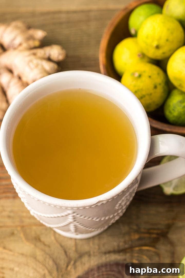 A mug of fresh ginger drink with some ginger and key limes on the side, emphasizing its comforting and natural essence.