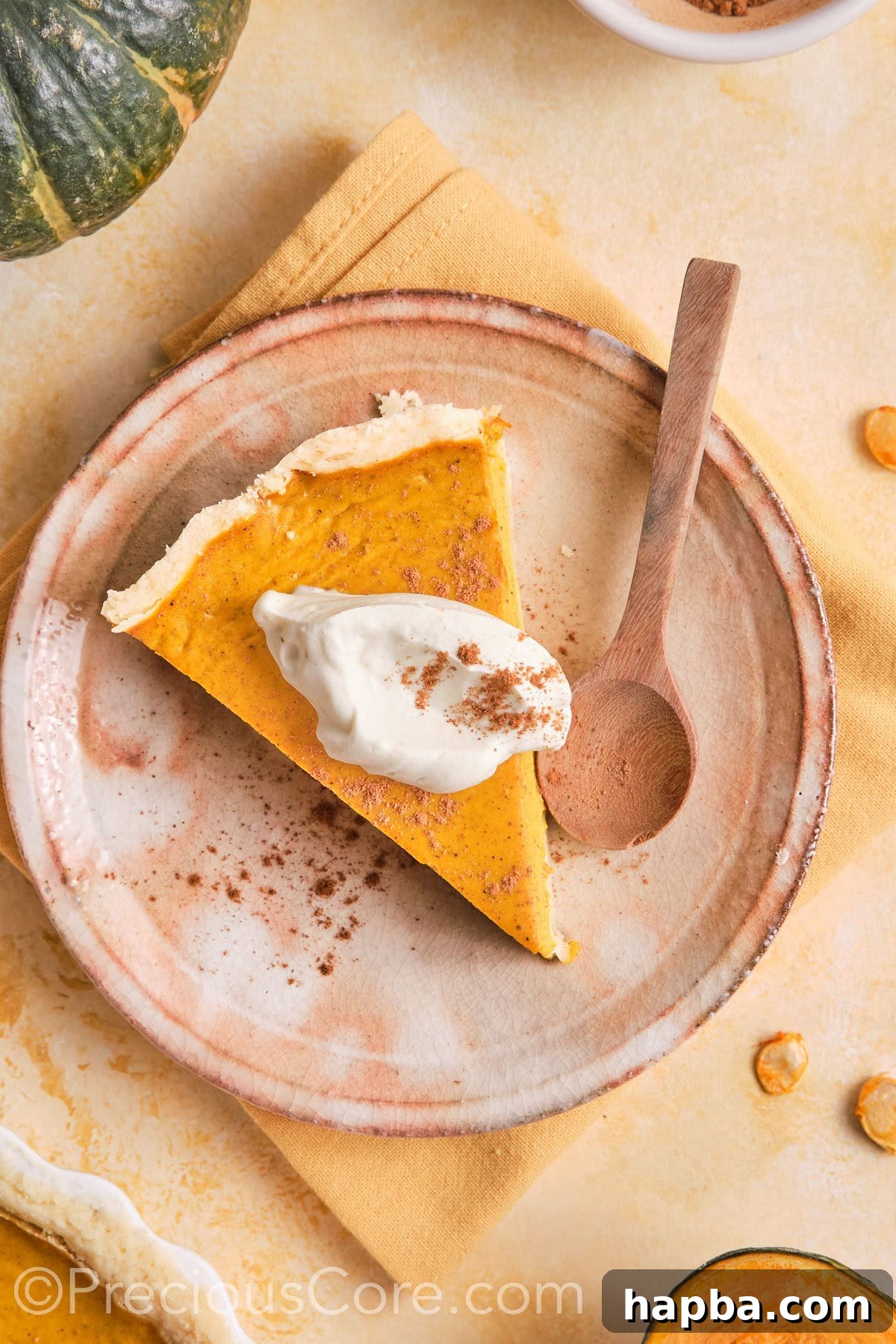 Pumpkin pie on a plate topped with cream and cinnamon.