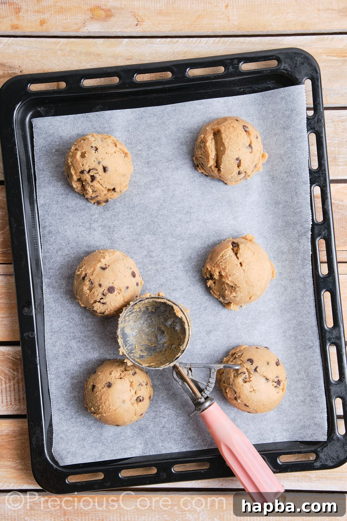 A baking sheet lined with parchment paper, holding six evenly spaced scoops of cookie dough.