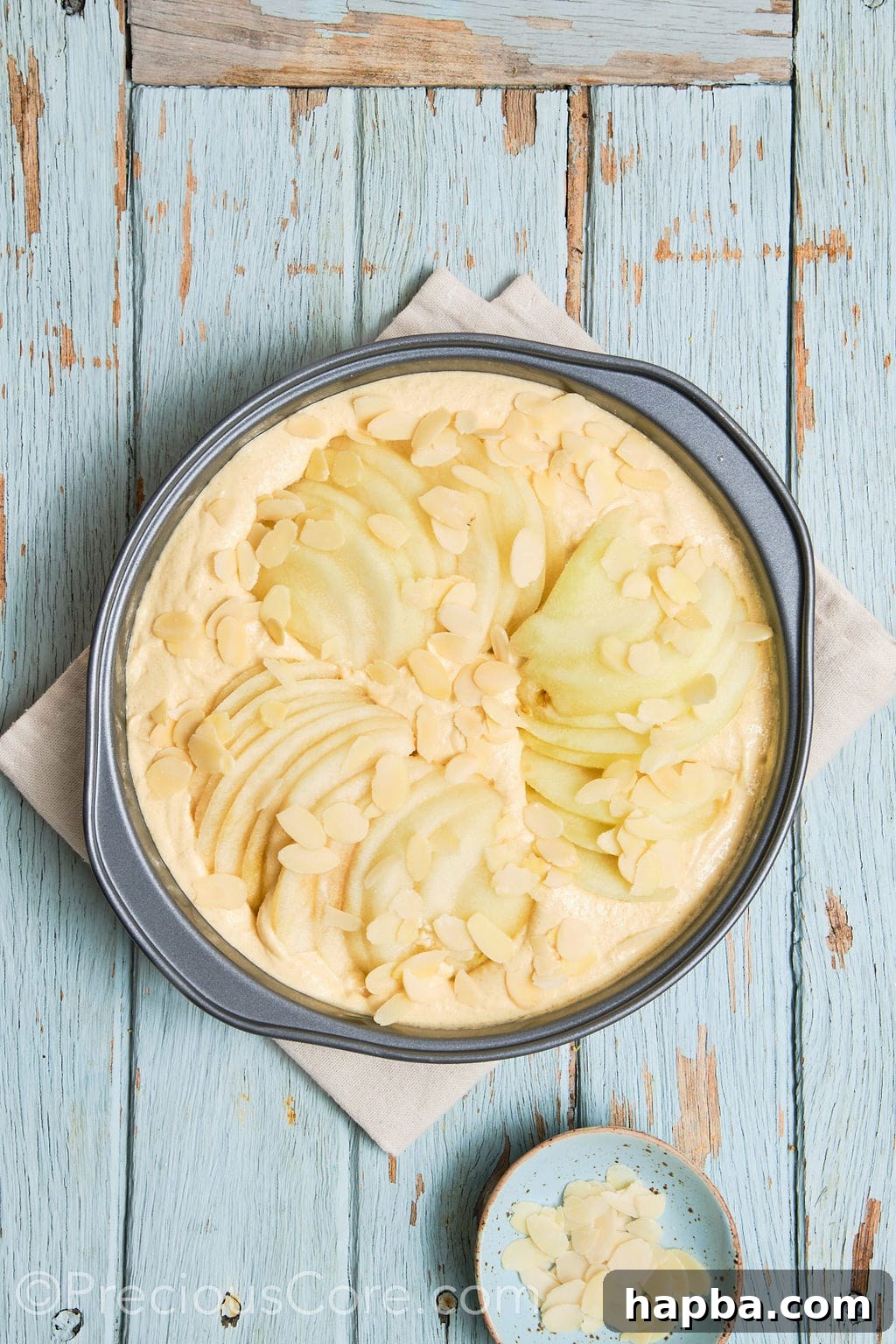 cake batter topped with sliced pears and almond flakes. 