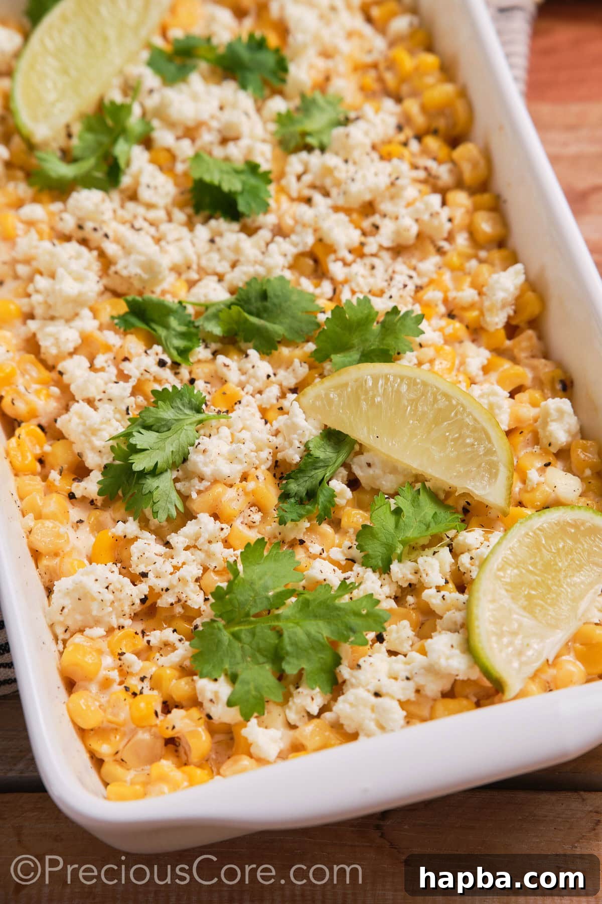 Creamy Elote Bake 9 Close-up of Mexican street corn casserole generously topped with crumbled queso fresco and fresh lime wedges.