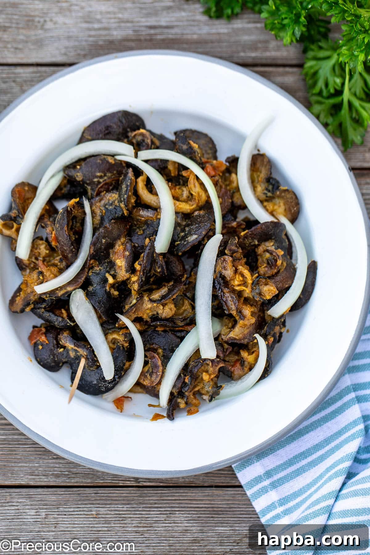 Authentic Cameroonian Snail Dish 2 Cameroonian snails on a white plate topped with sliced onions.