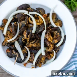Authentic Cameroonian Snail Dish 5 Cameroonian snails on a white plate topped with sliced onions.