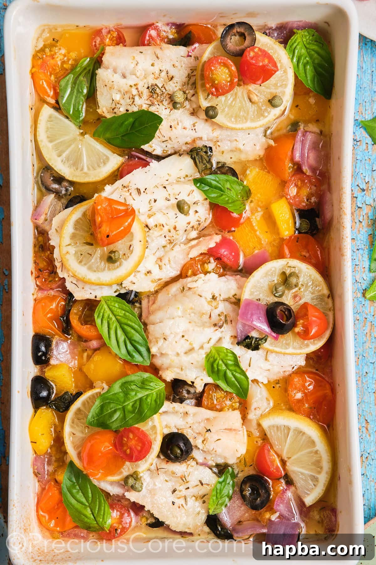 A baking dish filled with perfectly cooked Mediterranean baked fish, surrounded by roasted cherry tomatoes, olives, bell peppers, and lemon slices.